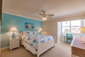 A bedroom with a bed, two bedside tables, a desk, a chair, a ceiling fan, and a window.