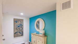 A bathroom with a bench, a vanity with a mirror, and a wall with a blue accent.