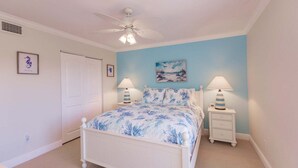 A bedroom with a bed, two bedside tables with lamps, a ceiling fan, and a door.