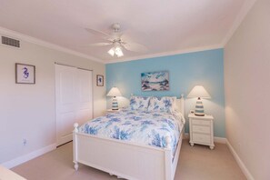 A bedroom with a bed, two bedside tables with lamps, a ceiling fan, and a door.