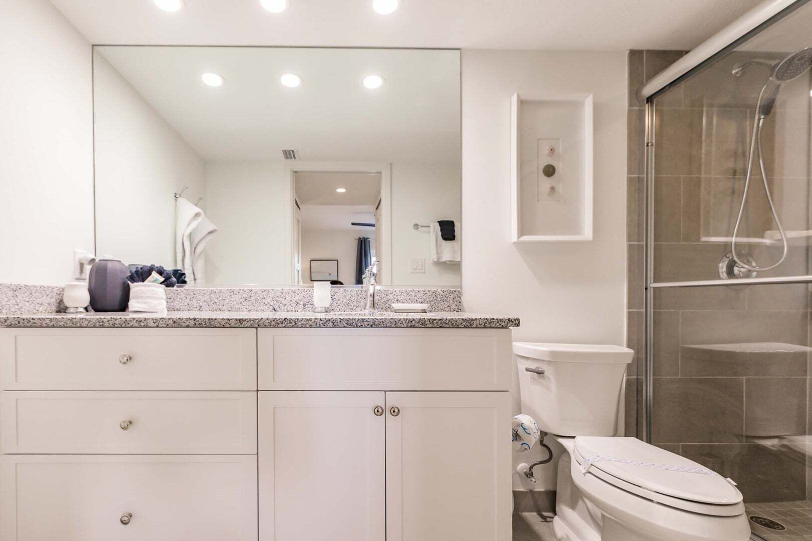 A modern bathroom with a large mirror, a granite countertop, a toilet, and a shower enclosure.