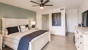 A bedroom with a bed, nightstands, a ceiling fan, a dresser, and a door leading to another room. - 1125-407 - Premium Plus - Step into Coastal Paradise (Siesta Key)