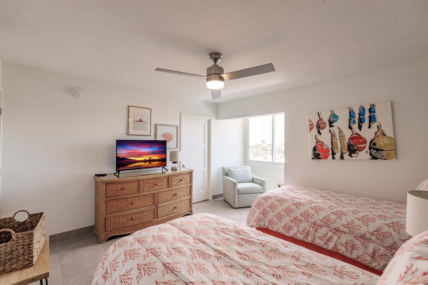 Una camera da letto con una televisione sul comò, una ventola a soffitto, una sedia e un letto con copriletto decorato.