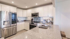 A modern kitchen with stainless steel appliances, white cabinetry, granite countertops, and a built-in oven. - 1125-407 - Premium Plus - Step into Coastal Paradise (Siesta Key)