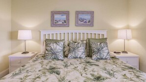 A bedroom with a bed, two nightstands, two lamps, and two framed pictures on the wall.