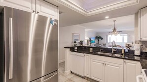 A modern kitchen with a stainless steel refrigerator, white cabinetry, and a black countertop.