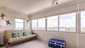 A room with a sofa, a window with blinds, a blue suitcase, and a wall-mounted light fixture.