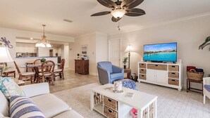 A living room with a sofa, a coffee table, a television, and a ceiling fan.