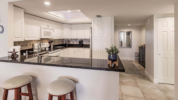 A modern kitchen with white cabinetry, a black countertop, and a central island with stools.
