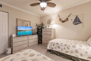 A bedroom with a TV, dresser, two beds, a ceiling fan, and wall decorations.