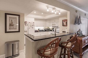 A kitchen with white cabinets, a central island with bar stools, a stainless steel refrigerator, and a microwave.