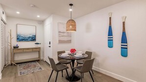 A dining area with a round table, four chairs, a hanging light fixture, and two wall-mounted paddleboards. - 1156 PD - Premium - Luxuriously Renovated Oasis (Siesta Key)