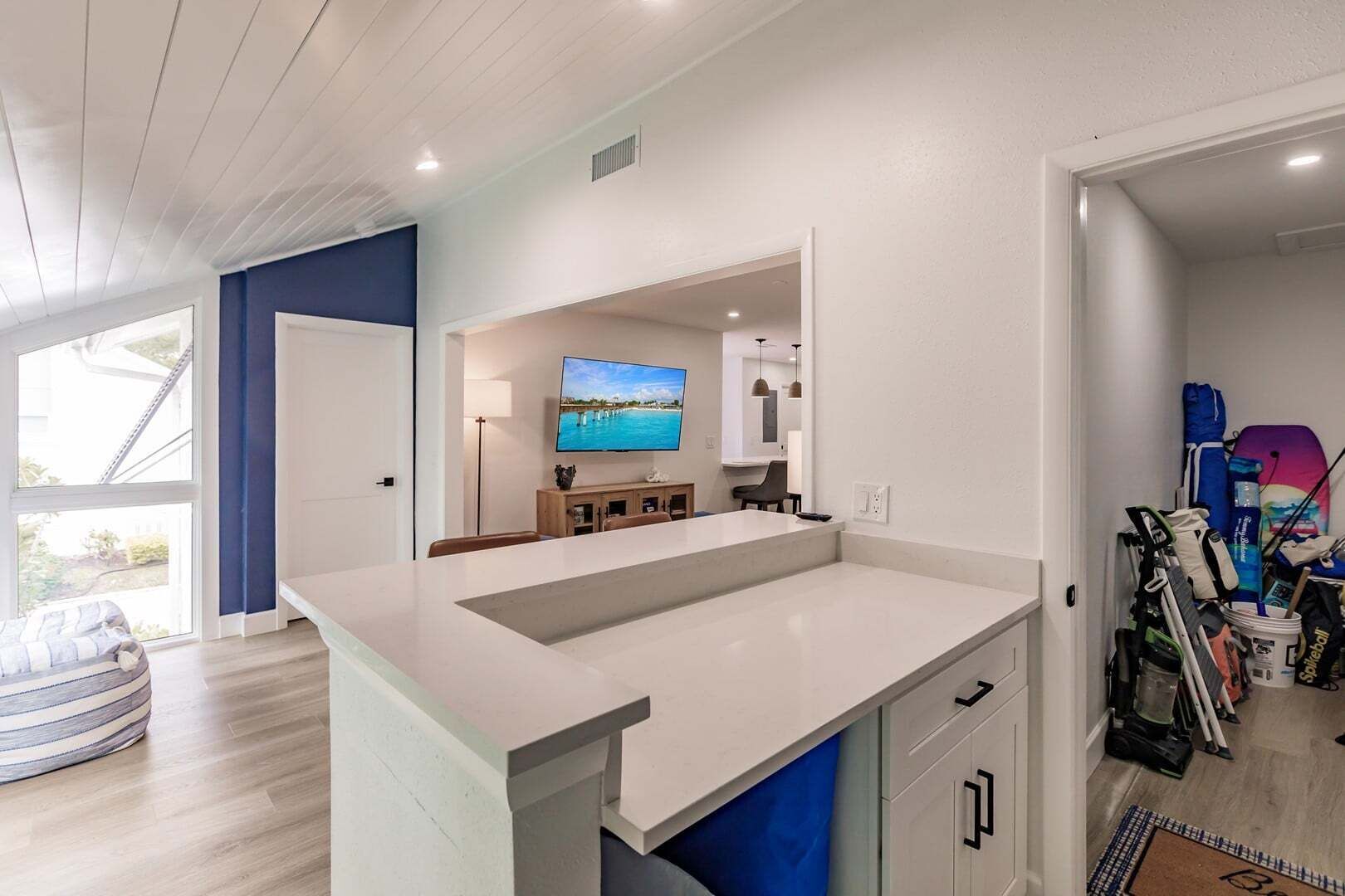 A modern kitchen with a large island, a dining area with chairs, a television, and a view of the outdoors.