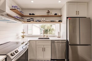 Une cuisine moderne avec des meubles blancs, des appareils en acier inoxydable et une fenêtre donnant sur un espace verdoyant.