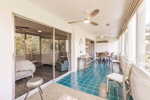 A spacious room with a large sliding glass door leading to an outdoor area, a ceiling fan, a dining table with chairs, and a small round table with a lamp.