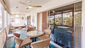 Une pièce dotée d’une grande porte vitrée donnant sur un jacuzzi, d’un ventilateur de plafond et d’un coin repas avec des meubles en osier.