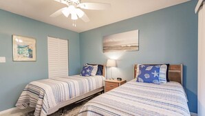A bedroom with two beds, a ceiling fan, a nightstand with a lamp, and a framed picture on the wall. - 1200-402 - Premium - Experience Serenity Steps from the Water (St. Petersburg)