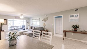 A spacious living area with a dining table, a sofa, and a coffee table. There is a sign on the wall that reads 'RELAX YOU'RE ON a nice day.' - 1200-402 - Premium - Experience Serenity Steps from the Water (St. Petersburg)