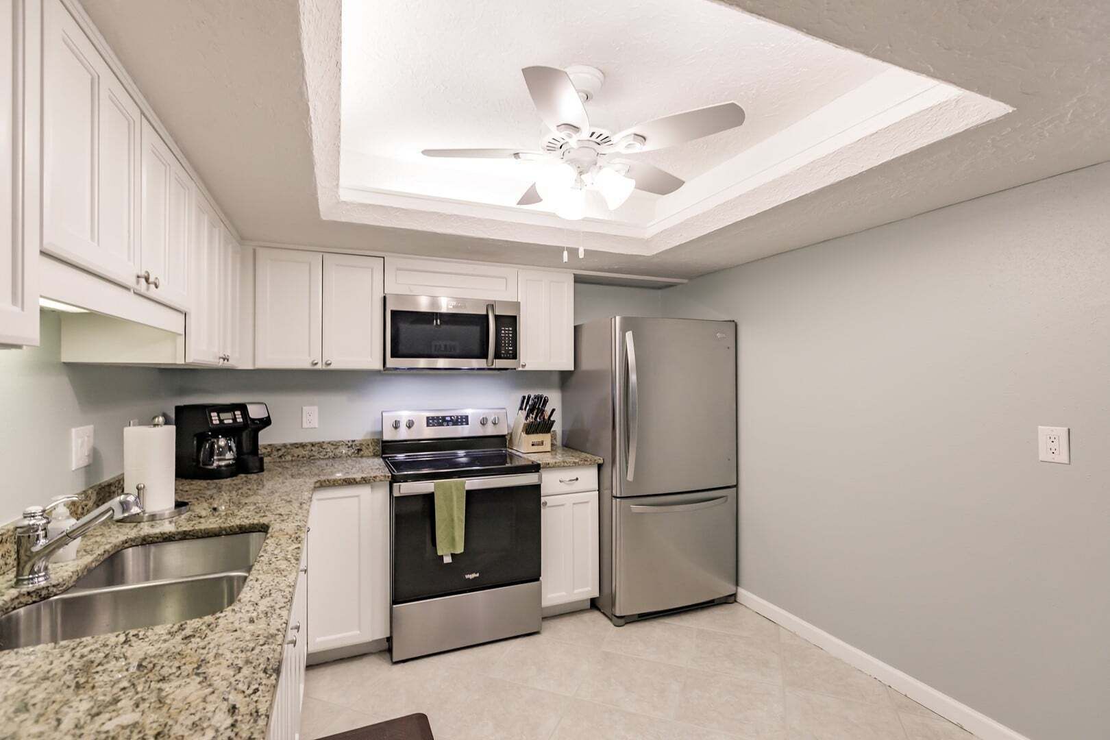 A modern kitchen with white cabinets, stainless steel appliances, a granite countertop, and a ceiling fan.