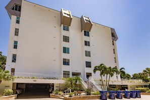 A multi-story hotel with a flat facade, a central staircase, and a parking area with trash bins.