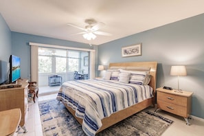 Une chambre à coucher comprenant un lit, des tables de chevet, un bureau, une chaise, un ventilateur de plafond et une fenêtre.