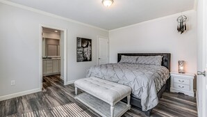 Een slaapkamer met een groot bed, een bankje, een nachtkastje, een kunstwerk aan de muur en een deur naar de badkamer.