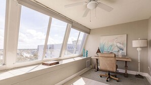 A room with a large window, a ceiling fan, a desk with a chair, a lamp, and a painting on the wall. - 1200-602 - Premium Plus -Enjoy Relaxing Bayfront Bliss (St. Petersburg)