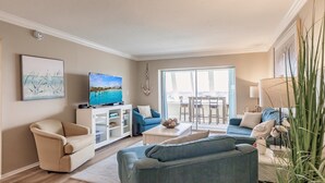 A living room with a television, a sofa, a chair, a cabinet, and a dining area with a table and chairs. - 1200-602 - Premium Plus -Enjoy Relaxing Bayfront Bliss (St. Petersburg)
