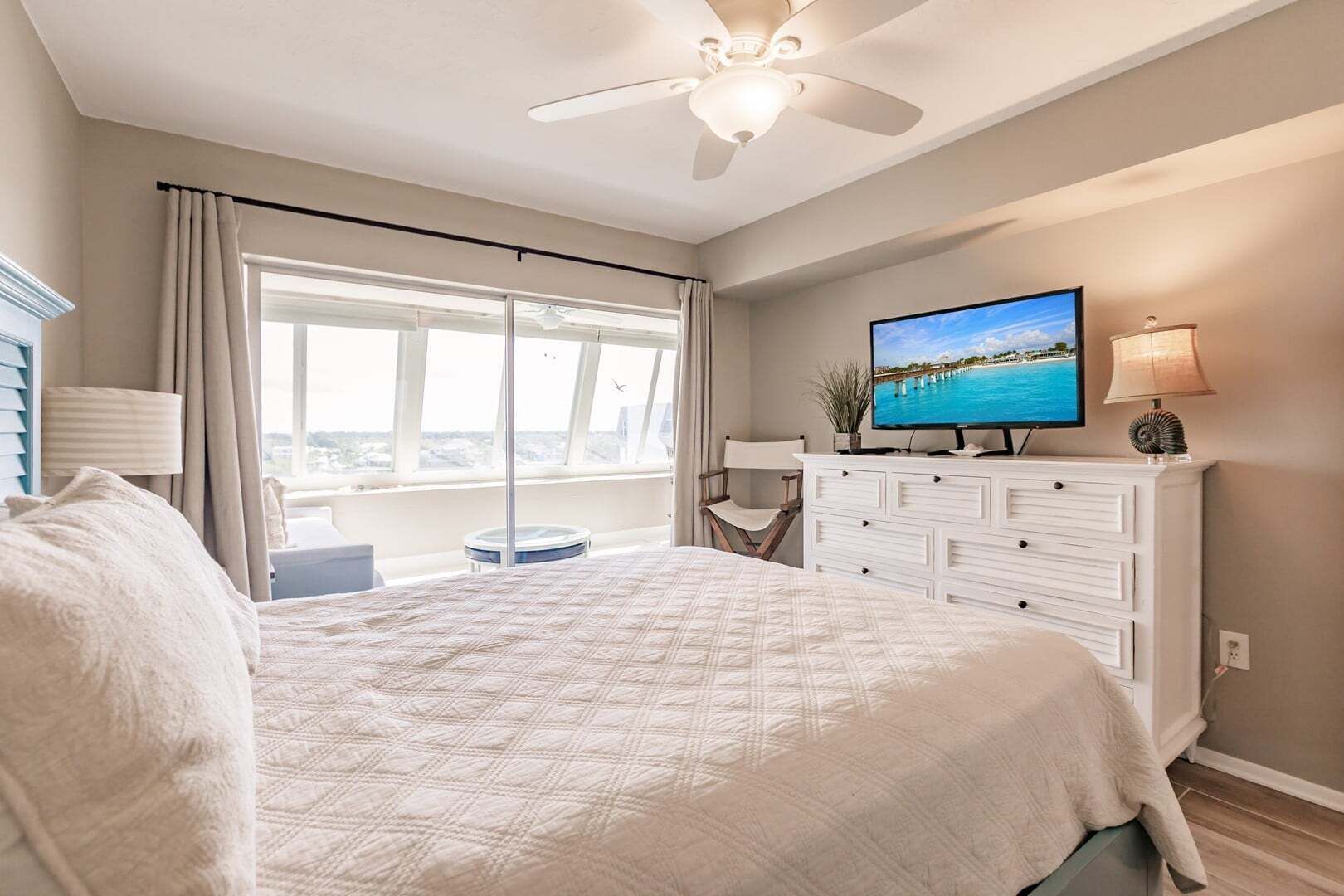 A bedroom with a large bed, a television, a dresser, and a view of the ocean through a large window.