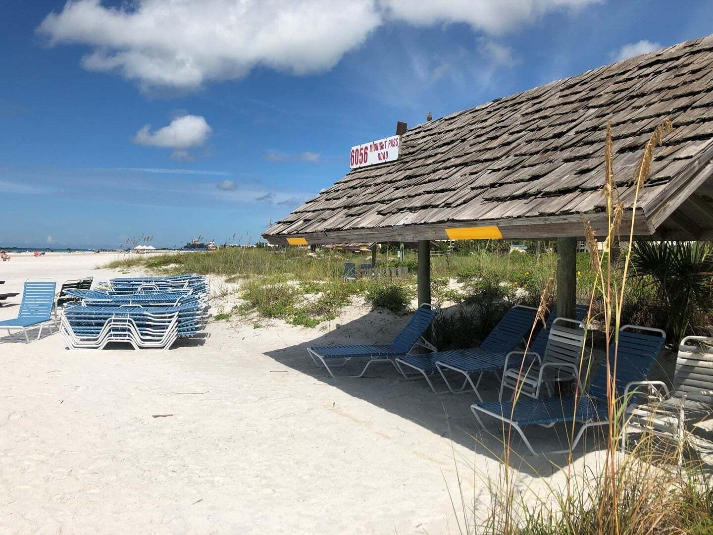 A beach with a wooden structure, a sign indicating a road, and rows of blue lounge chairs.