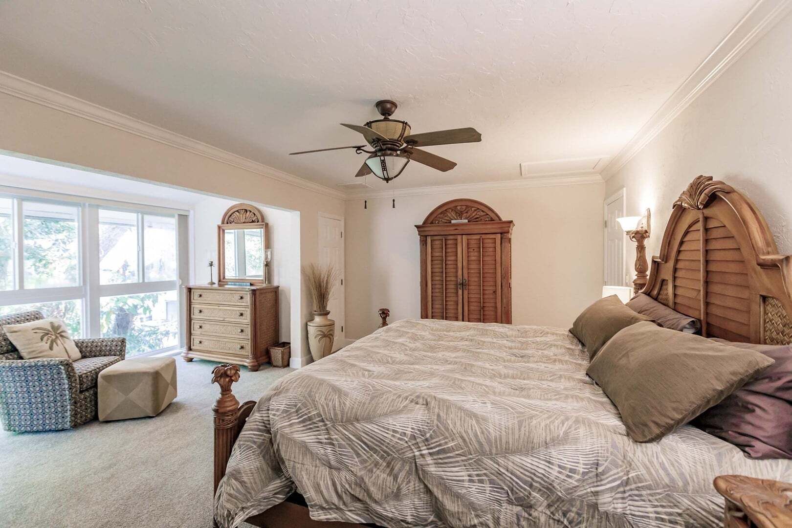A bedroom with a large bed, a ceiling fan, a dresser, a mirror, and a window.