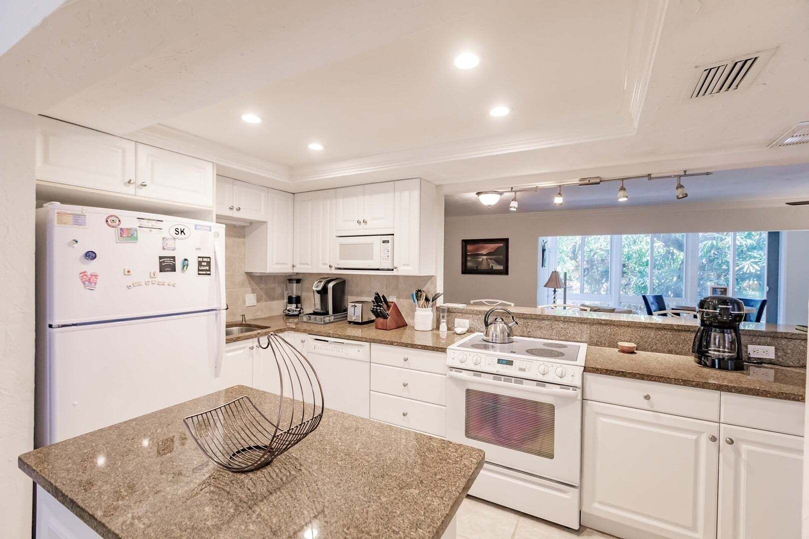 A modern kitchen with white cabinets, a granite countertop, a built-in microwave, a stove, and a coffee maker.