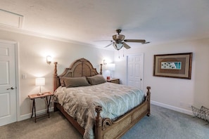 Ein Schlafzimmer mit einem hölzernen Bett, Deckenventilator, Nachttischlampen, einem gerahmten Bild an der Wand und Teppichboden.