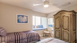 Una camera da letto con due letti, una panca finestrata con una poltrona, un armadio e una ventola a soffitto.