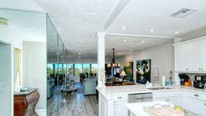 A modern kitchen with white cabinetry, a large island, and a view through glass doors to an outdoor seating area.