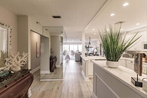 A modern kitchen with a central island, a dining area, and a hallway leading to a living space.