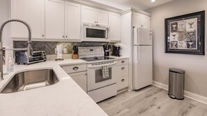 Una cucina moderna con mobili bianchi, elettrodomestici in acciaio inossidabile, un forno a microonde, un piano cottura e un frigorifero.