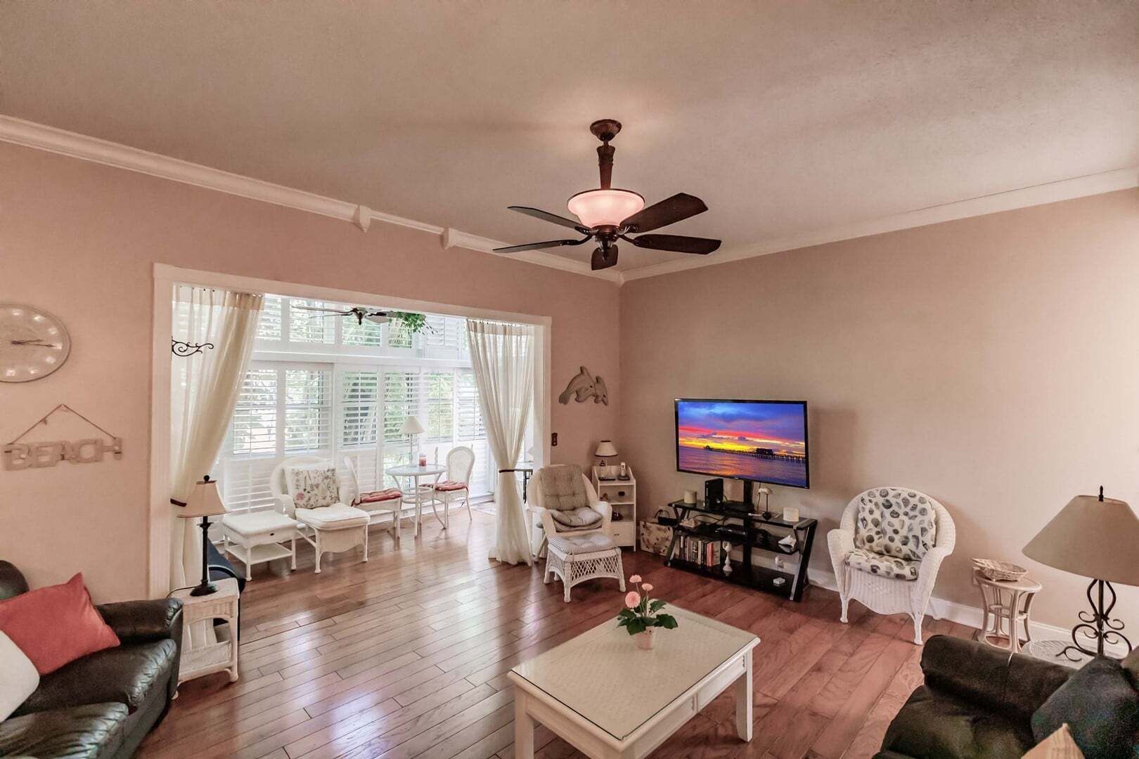 A living room with a ceiling fan, a flat-screen TV, and a large window with curtains.