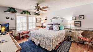 Une chambre à coucher comprenant un lit, un bureau, une chaise, un ventilateur de plafond et une fenêtre avec des stores.