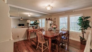 Un coin repas avec une table et des chaises en bois, un ventilateur de plafond et une fenêtre avec des stores.