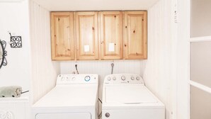 Une buanderie équipée de deux machines à laver à chargement frontal, de couleur blanche, et de meubles de rangement en bois placés au-dessus.