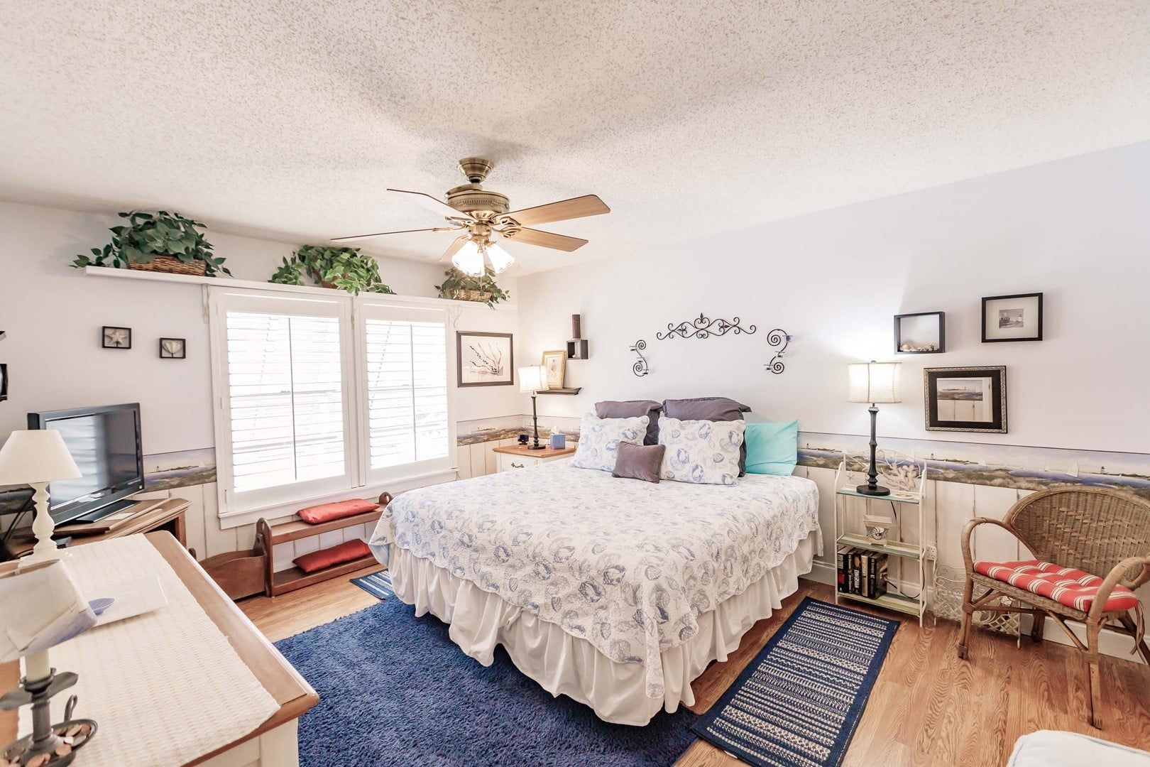 A bedroom with a bed, a desk, a chair, a television, and a ceiling fan.