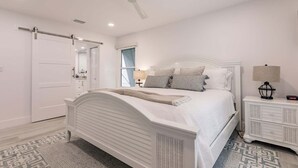 A bedroom with a bed, a nightstand, a lamp, a ceiling fan, and a window. - 6042 - Premium Plus-Ultimate Vacation Haven (Sarasota)