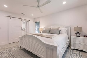 Une chambre à coucher avec un lit, une table de chevet, une lampe, un ventilateur de plafond et une fenêtre.