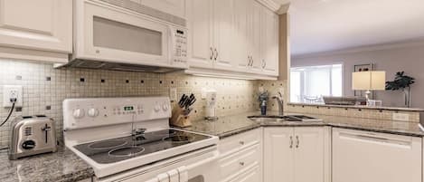 Une cuisine moderne avec des meubles blancs, un four à micro-ondes encastré, une cuisinière et un lave-vaisselle.