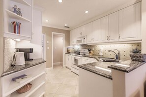 A modern kitchen with white cabinetry, granite countertops, a built-in oven, microwave, and a sink with a faucet.