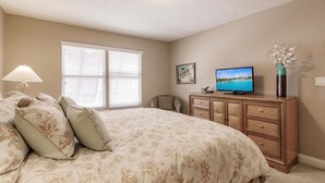 A bedroom with a large bed, a dresser, a television, and a window with blinds.