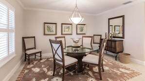 A dining room with a glass table surrounded by chairs, a chandelier, framed artwork on the walls, and a large mirror.