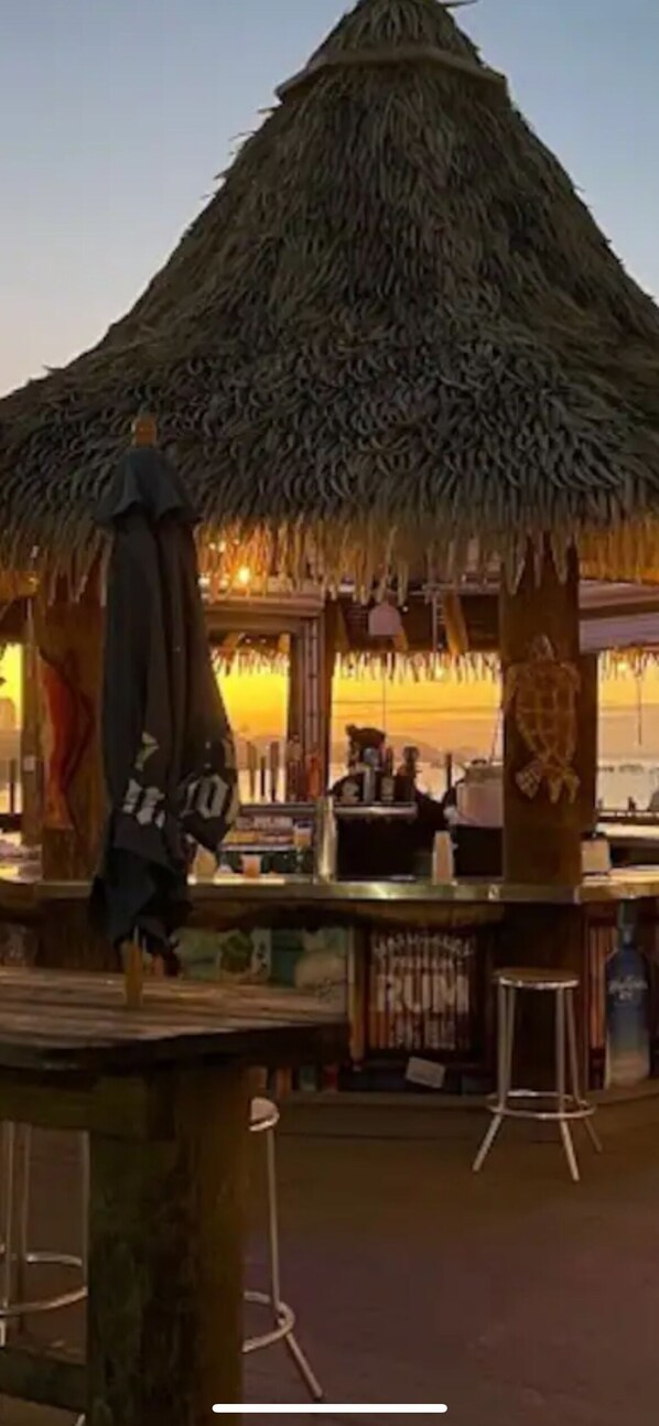 Una estructura con techo de paja que incluye una zona de bar, taburetes y una persona de pie cerca.