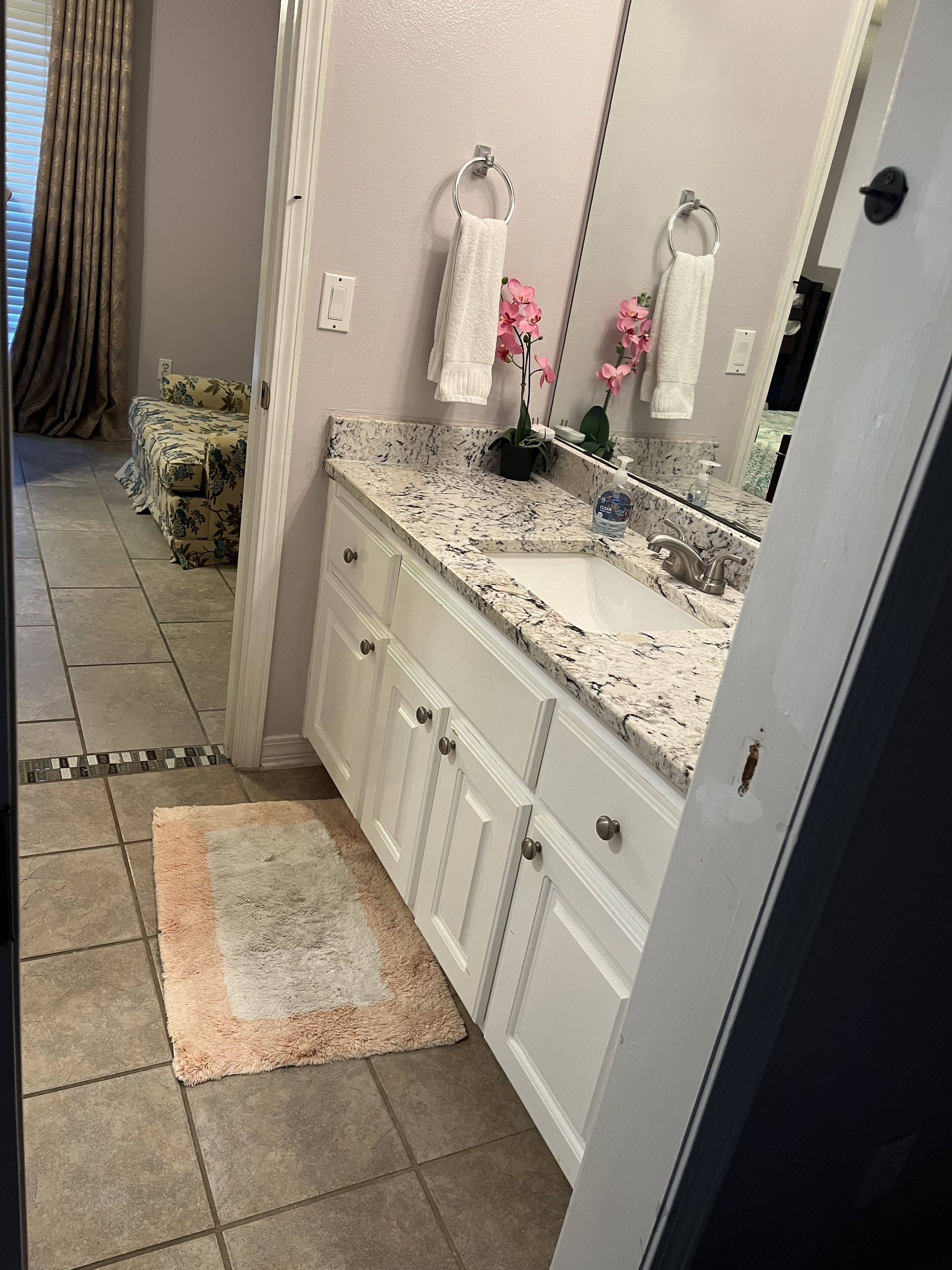 A bathroom with a marble countertop, white cabinets, a sink, and a mirror.